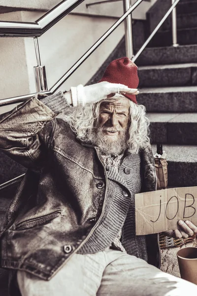 Caucasian old homeless man seeing friend distantly and watching him.