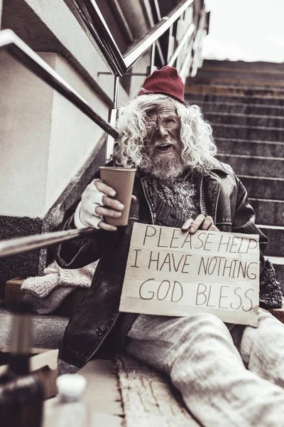 Desperate beggar sitting outside and writing poster asking for help. — Stock Photo, Image