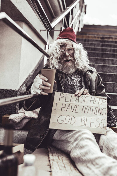 Desperate beggar sitting outside and writing poster asking for help.