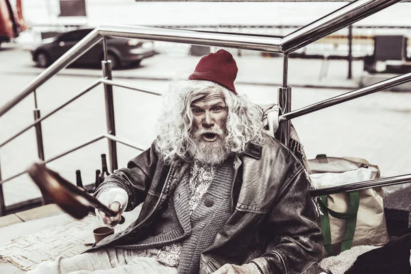 Angry almsman sitting and threatening strangers with cane. — Stock Photo, Image