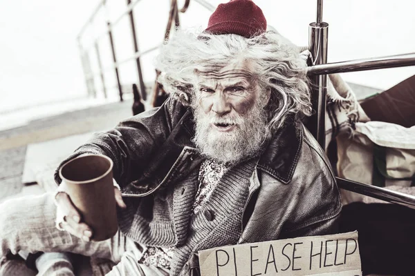 Stray elderly sitting near railing and sticking for strangers.