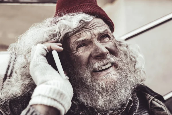 Porträt eines Obdachlosen, der mit dem Smartphone spricht und in den Himmel blickt. — Stockfoto