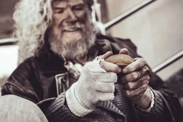 Caucasian homeless man happy to get a bun and holding it with both hands.