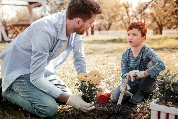 Profesor serio mostrando cómo plantar flores amarillas en el patio trasero de la escuela — Foto de Stock