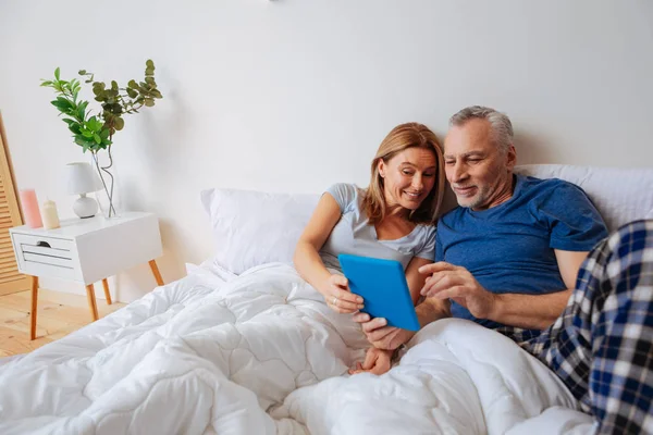 Marido de cabelos grisalhos e sua esposa lendo notícias no tablet — Fotografia de Stock