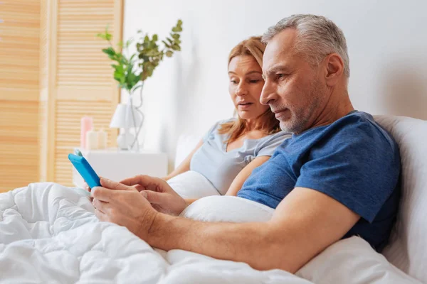 Grauhaariger Ehemann zeigt seiner Frau Morgennachrichten auf Tablet — Stockfoto