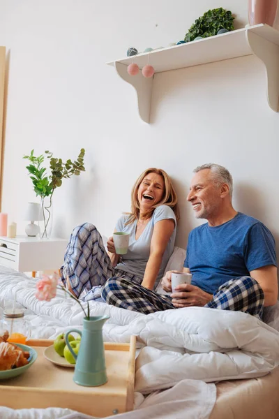 Esposa y marido se sienten alegres desayunando en el dormitorio — Foto de Stock