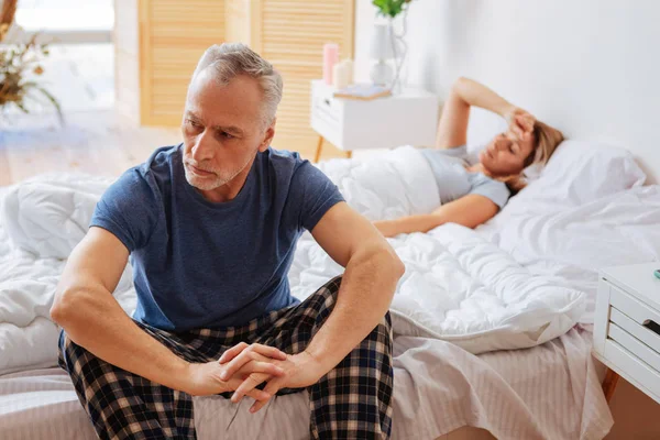 Esposo sentado en la cama mientras su esposa duerme en la mañana — Foto de Stock