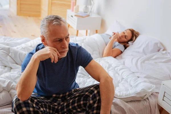 Preocupado marido enojado sentado en la cama cerca de la esposa dormida — Foto de Stock