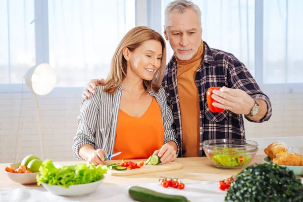 Bärtiger Ehemann bringt Paprika für Frau, die Salat kocht — Stockfoto