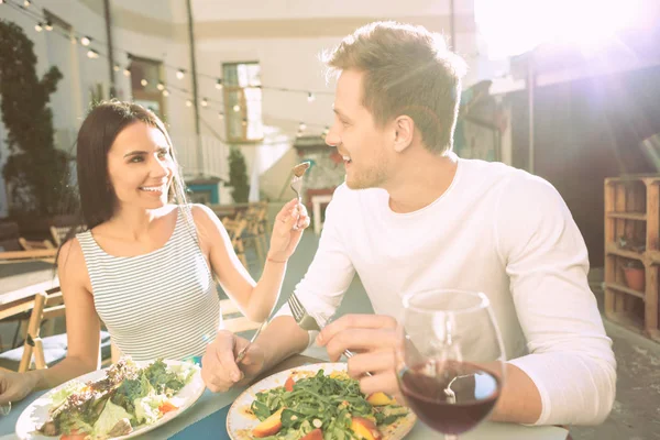 Attractive long-haired lady with wide smile feeding her boyfriend