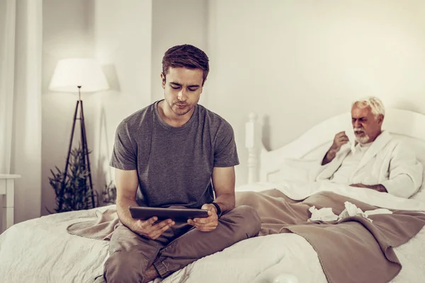 Preocupado masculino segurando tablet enquanto seu avô doente tosse — Fotografia de Stock