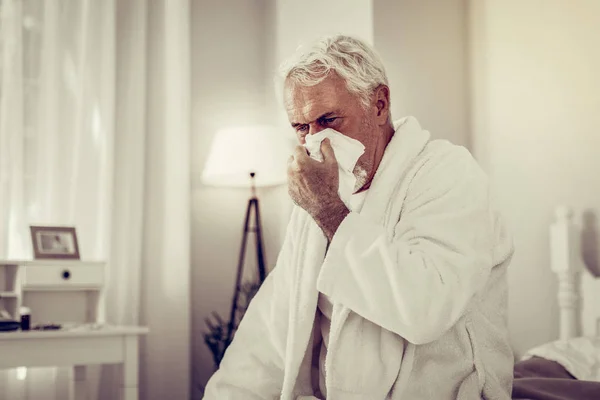 Öreg beteg ember fúj az orrát, papír zsebkendő használata — Stock Fotó