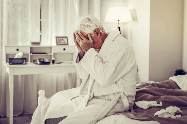 Άρρωστος άνθρωπος κλείσιμο πρόσωπο με τα χέρια και να κάθεται στο κρεβάτι — Φωτογραφία Αρχείου