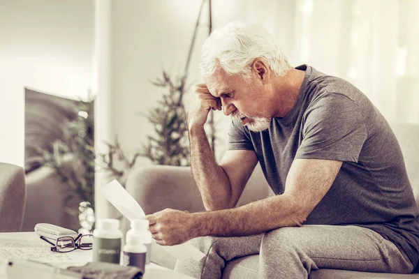 Envelhecimento senhor segurando sua cabeça em desespero enquanto segurando papéis — Fotografia de Stock
