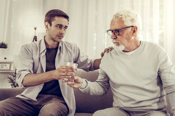 Supporting man handing the glass of water to elderly mister — Stock Photo, Image