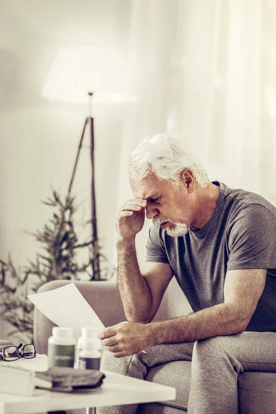 Aged mister sitting on sofa and clutching head in shock — Stock Photo, Image