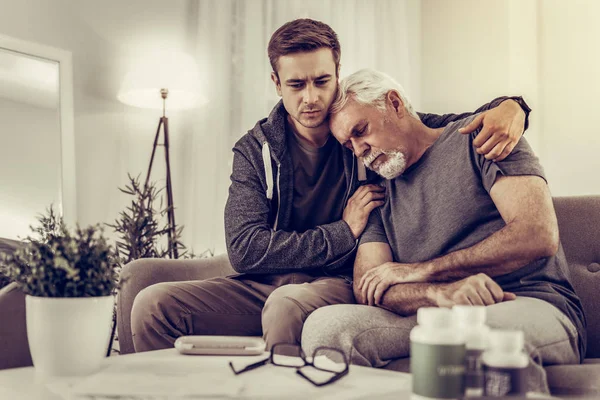 Heartsore neto abraçando e confortando seu avô de cabelos prateados idosos — Fotografia de Stock