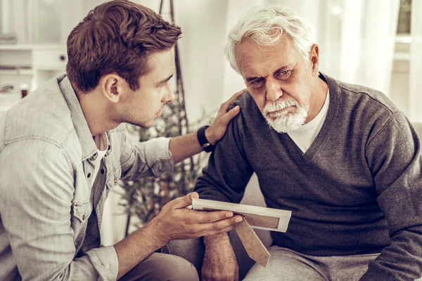 Adult son showing to his old father a family photo.