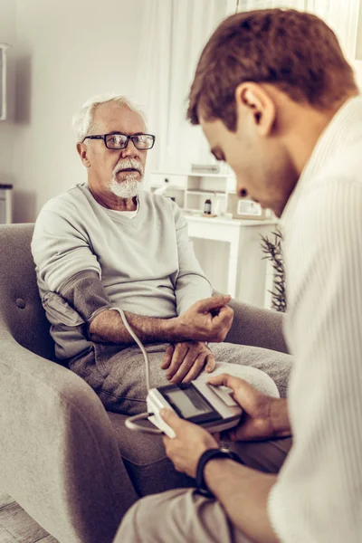 Volwassen zoon zorgvuldig nemen de bloeddruk van zijn vader — Stockfoto