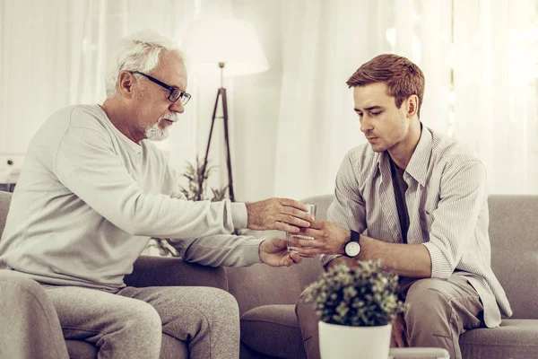 Helpful man handing the glass of water to elderly mister — Stock Photo, Image