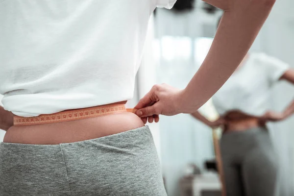 Young woman measuring a waist near the mirror — Stock Photo, Image