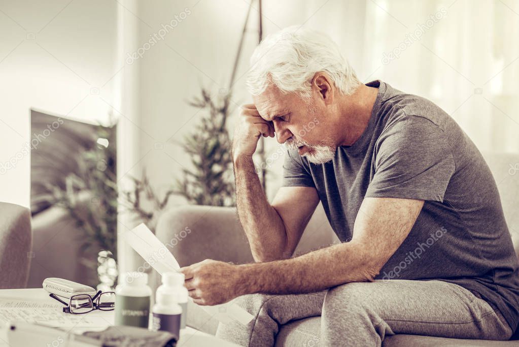 Aging mister clutching his head in despair while holding papers
