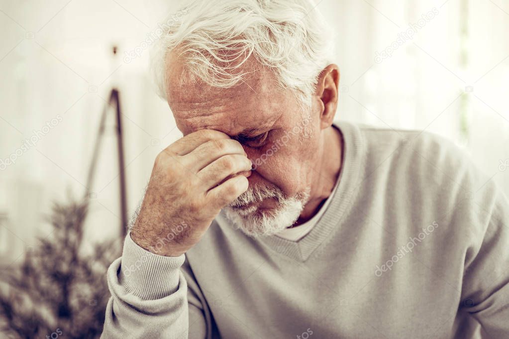 Old sick grey-haired man in beige sweater feeling terrible pain