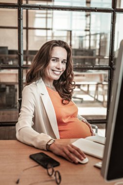 Büyük ruh halinde iş yerinde otururken neşeli uzun saçlı kadının