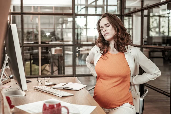 Suffering good-looking woman having backache on working place — Stock Photo, Image