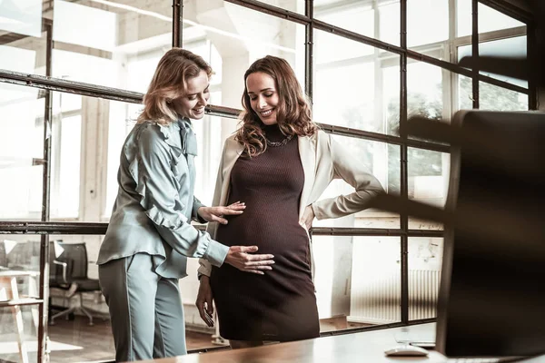 Strahlende blonde Freundin reibt Schwangerschaftsbauch ihres dunkelhaarigen Kollegen — Stockfoto