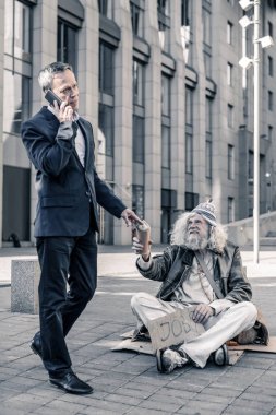 Kayıtsız zengin adam smartphone üzerinde konuşmak ve para evsizlerle paylaşımı