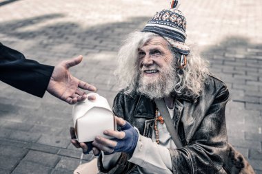 Dirty grey-haired senior homeless wearing ragged clothes and receiving food clipart