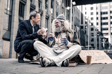 Beaming good-looking man having pleasant conversation with dirty homeless clipart