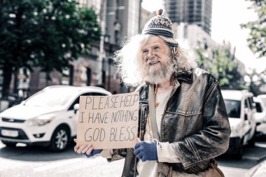 Miserable dirty old man being poor homeless and standing with cardboard clipart