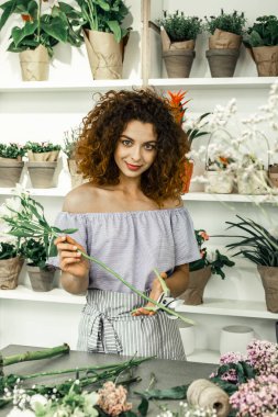 Mavi gözlü öğrenci yeşil dekorasyonlar tutan çiçek dükkanında çalışan