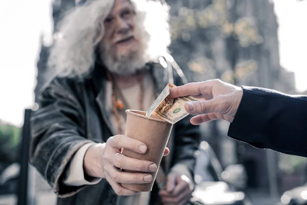 Šedá vlasy bezdomovec lepenkové Cupu přepravující a žebrání — Stock fotografie