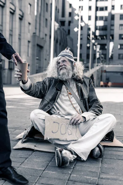 Long-haired dirty man sitting on cold ground with cardboard nameplate — Stock Photo, Image