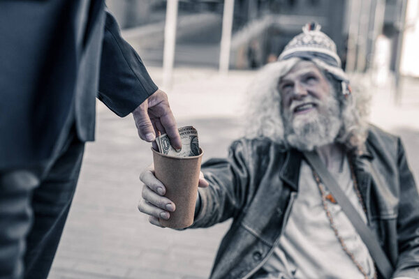 Thankful homeless man with dirty hair stretching empty coffee cup