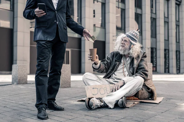 Usmívající se šedovlasé špinavé nezaměstnaný muž sedí na zemi — Stock fotografie