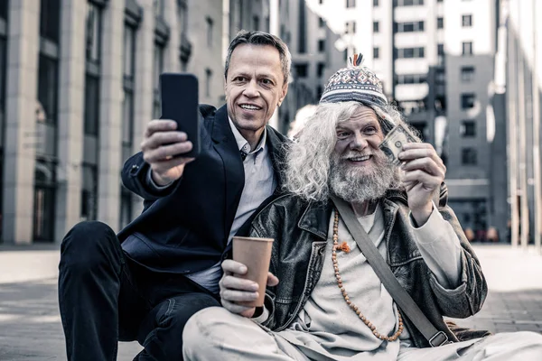 Alegre hombre de negocios de pelo corto haciendo foto con radiantes personas sin hogar — Foto de Stock