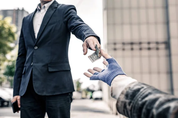 Generous good-looking man in dark costume sharing his money with homeless — Stock Photo, Image