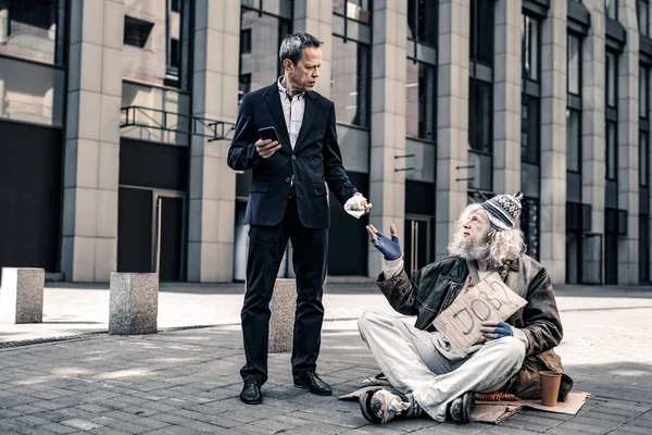 Verward korthaar man met smartphone uitvoering de helft van het broodje — Stockfoto