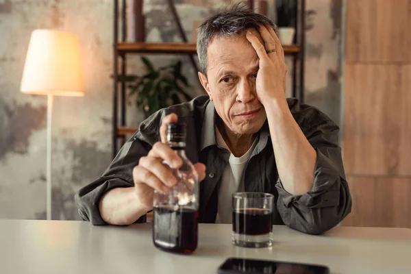 Antiguo alcohólico desesperado sentado frente a la botella de vidrio con rom —  Fotos de Stock