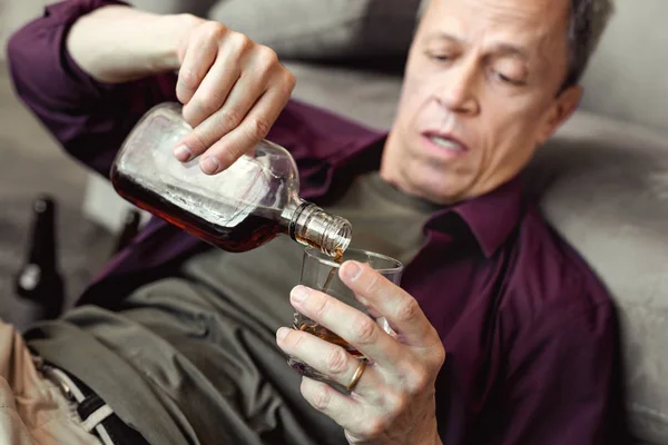 Беспомощный взрослый мужчина добавляет алкоголь в стакан — стоковое фото