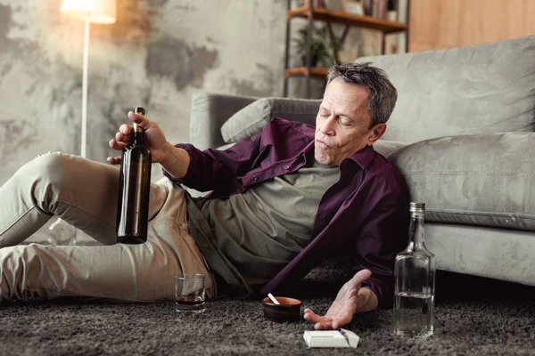 Borracho mal parecido alcohólico de pelo gris rodeado de botellas — Foto de Stock