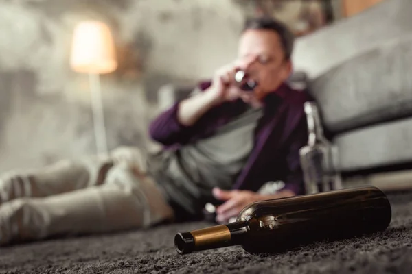 Uomo adulto sdraiato su tappeto in soggiorno con bottiglie vuote intorno — Foto Stock