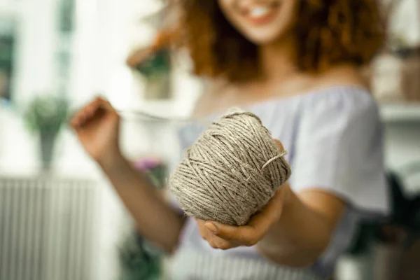 Close up of smiling florist holding beige clew while using it for bouquet