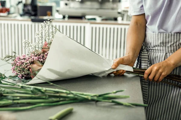 Florista vistiendo uniforme a rayas disfrutando del proceso de hacer ramo — Foto de Stock