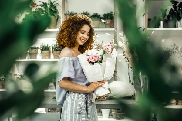 Jovem estudante trabalhando na loja floral segurando belo buquê — Fotografia de Stock